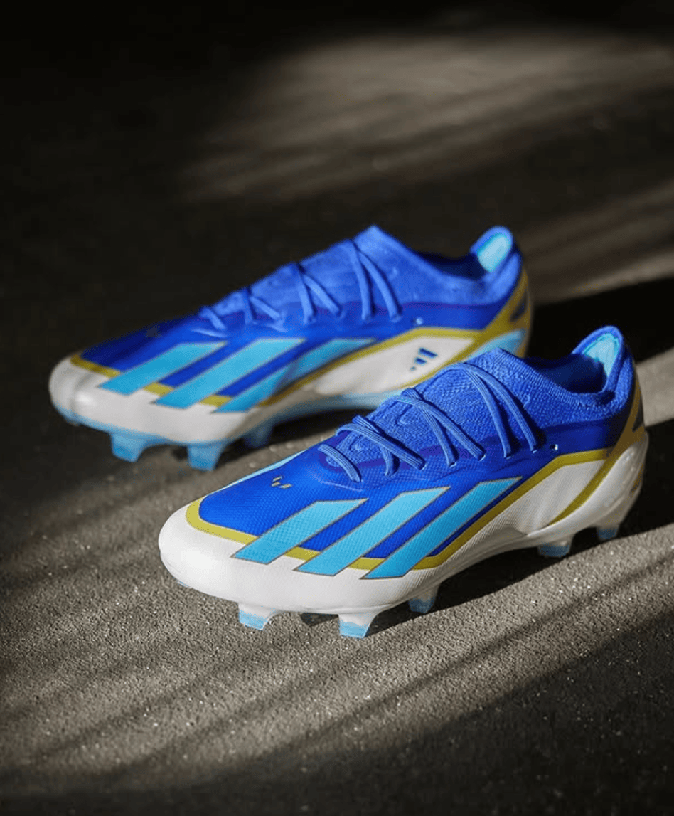 Screenshot_2025-01-21_184635 | UAE SPORT STORE Pair of bright blue soccer cleats with turquoise stripes and white toes, resting on a dark surface.