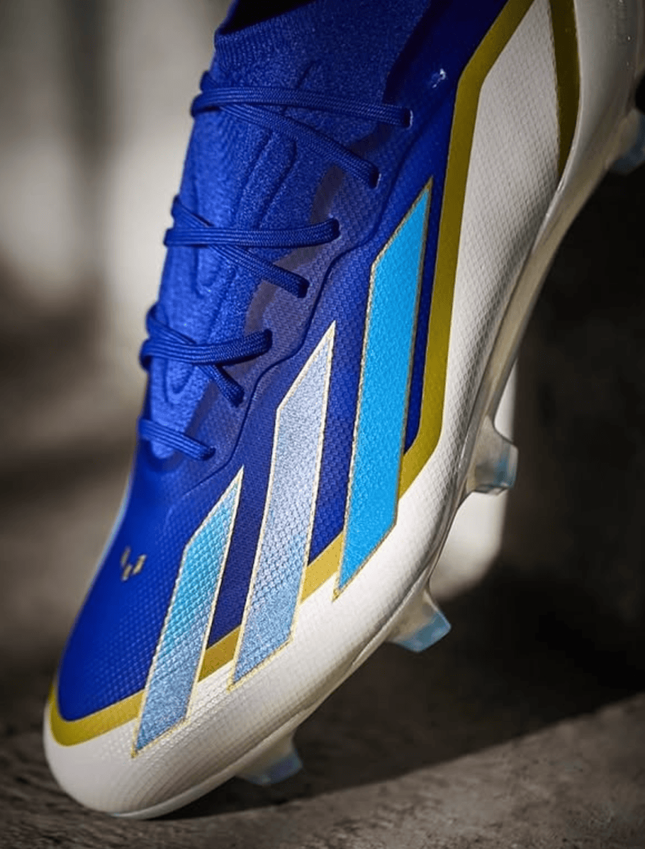 Screenshot_2025-01-21_184649 | UAE SPORT STORE Blue soccer cleat with light blue and gold geometric stripes on a white sole, close-up view of laces and upper panel(s).