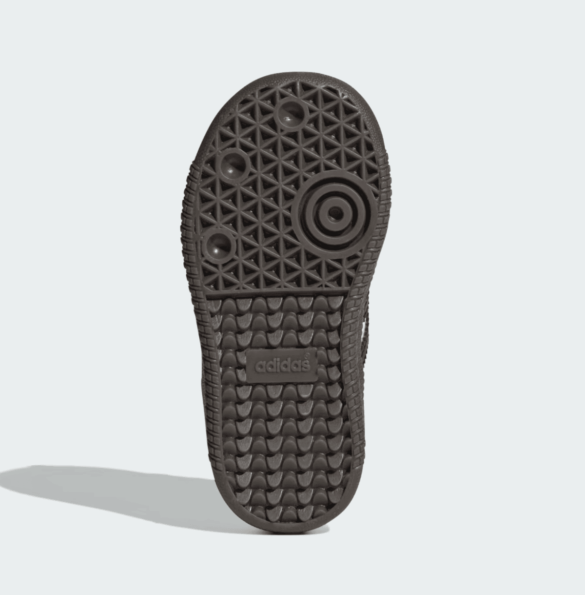 Bottom view of a dark brown Adidas sneaker sole with circular traction pattern and embossed Adidas logo near the arch area.