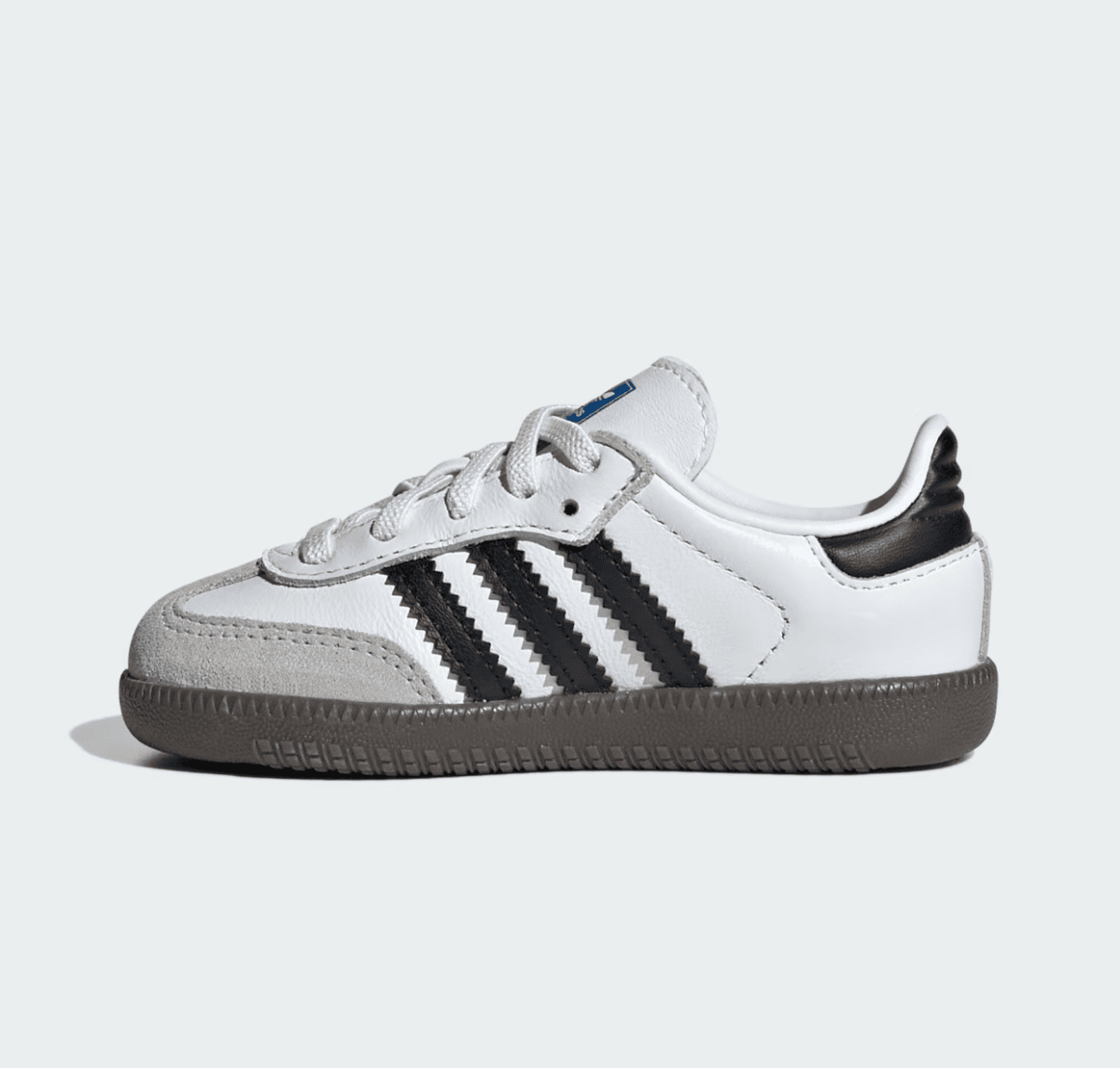 White low-top sneaker with black three stripes and gray suede toe cap on a brown sole (side view).