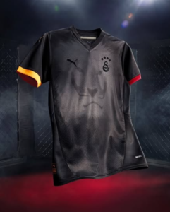 Black athletic jersey with orange trim on the left sleeve and red trim on the right, Puma logo on chest and a club crest with stars, set against a dark arena backdrop.