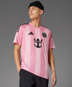 Person wearing a pink striped soccer jersey with a black crest, Adidas logo, and a black beanie against a gray backdrop.