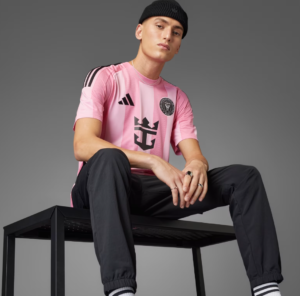 Portrait of a man in a pink striped football jersey and black beanie, sitting on a black bench against a gray background, looking at the camera.
