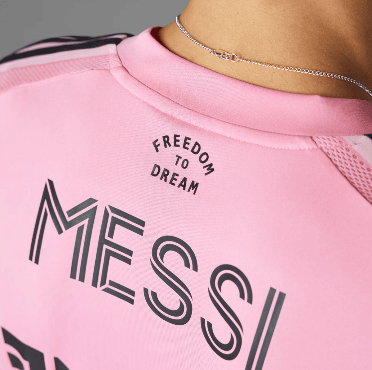 Close-up of a pink athletic shirt with the curved text 'FREEDOM TO DREAM' and a silver necklace visible at the neckline.