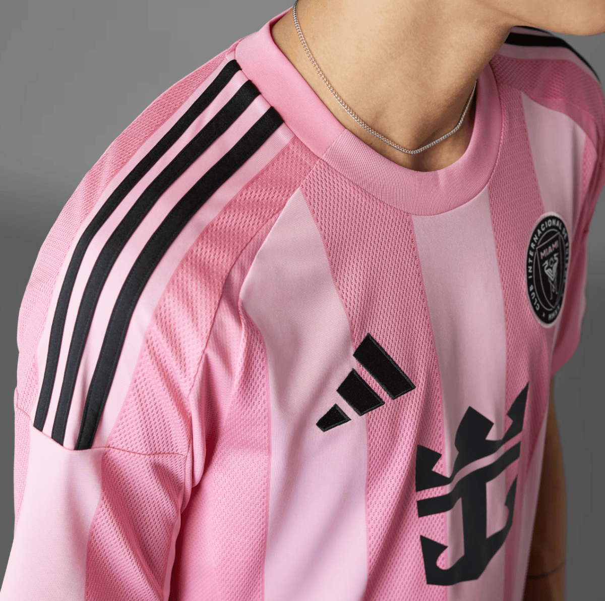 Close-up of a pink Adidas soccer jersey with black shoulder stripes, visible chest logo, and a chain necklace on the wearer's neck.
