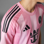 Close-up of a pink Adidas soccer jersey with black shoulder stripes, visible chest logo, and a chain necklace on the wearer's neck.