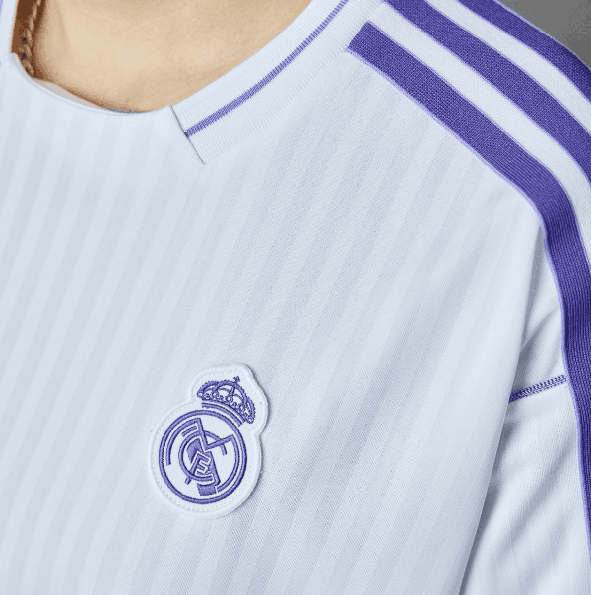 White Real Madrid jersey with purple trim and crest on the left chest (close-up).