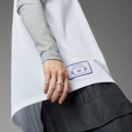 Close-up of a hand wearing a ring touching the hem of a white jacket with a Real Madrid tag, gray sleeve visible.