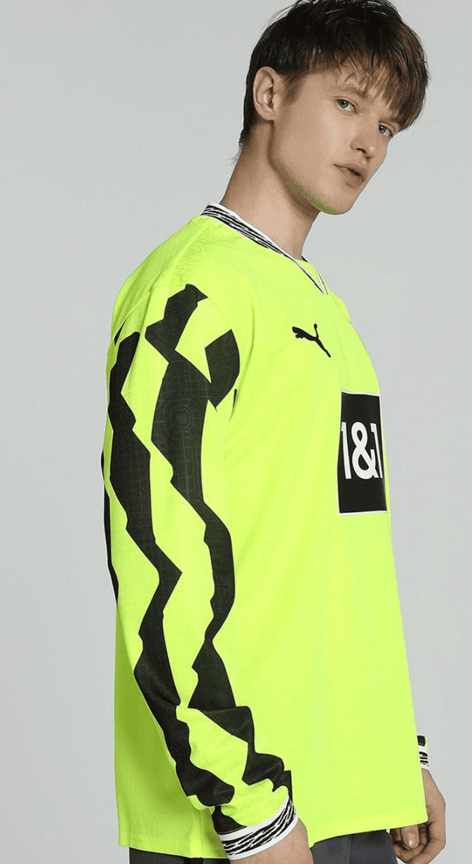 Screenshot_2025-04-13_053212 | UAE SPORT STORE Model wearing a neon yellow long-sleeve athletic jersey with bold black geometric sleeve graphics and a black sponsor patch on the chest (Puma logo visible).