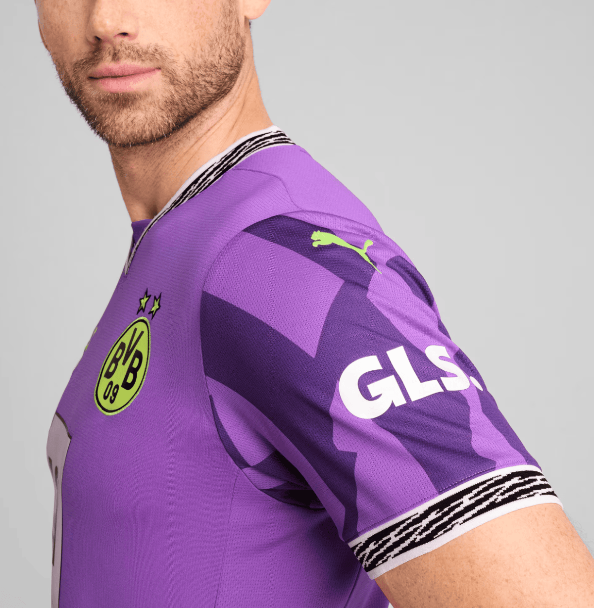 Close-up of a man wearing a purple Borussia Dortmund jersey, showing the club crest on the chest and neon green PUMA logo on the sleeve.