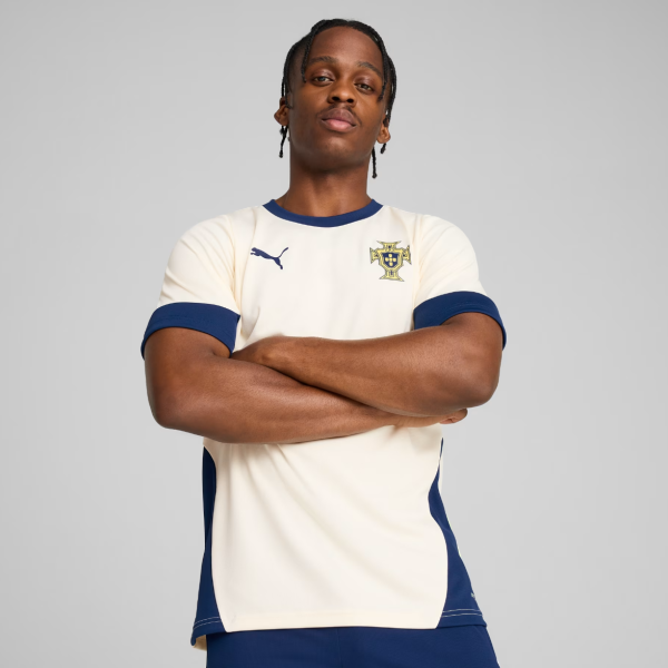 Male soccer player with arms crossed, wearing a cream and blue Portugal jersey.