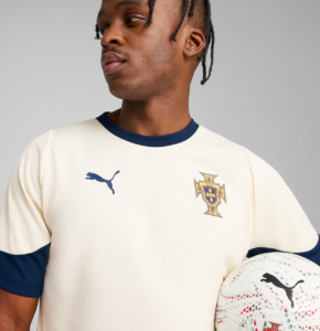 Close-up of a male soccer player in a cream Portugal jersey with navy trim, holding a white football with a blue Puma logo to the right.