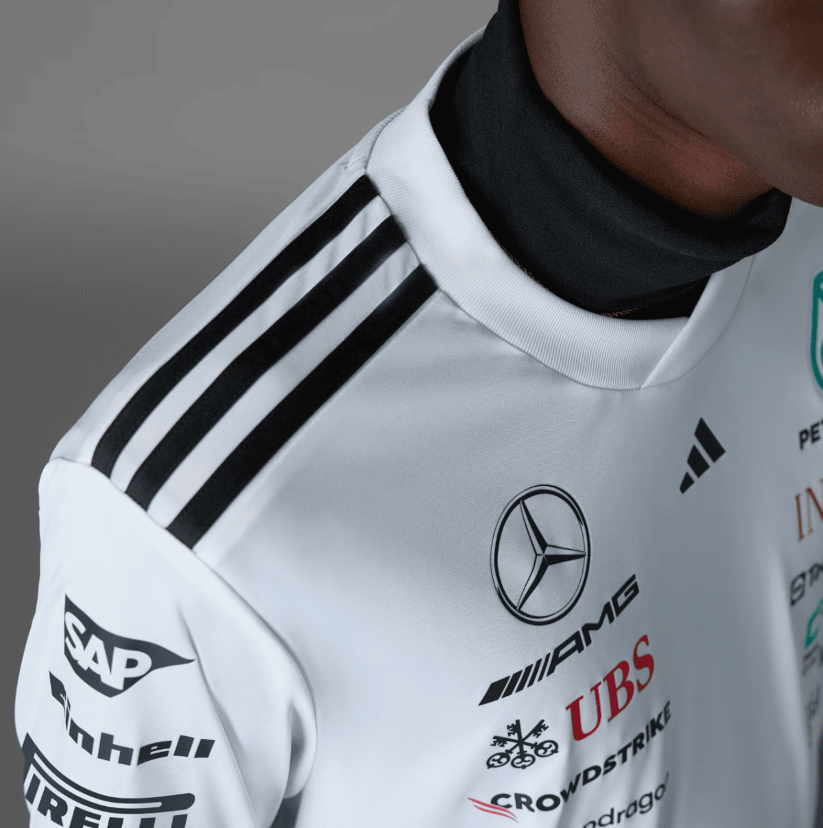Close-up of a white racing jersey with the Mercedes logo and sponsor patches, black underlayer at the neck, and black stripe accents on the shoulder.
