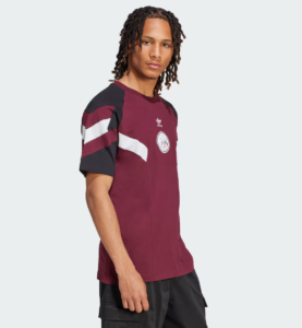 Man in a maroon Adidas T‑shirt with white stripe details on the sleeves and a circular chest emblem, shown in profile.