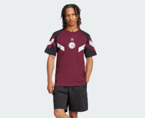 Male model wearing a burgundy Adidas color-block short-sleeve tee with black sleeves and a circular chest emblem, paired with black cargo shorts.