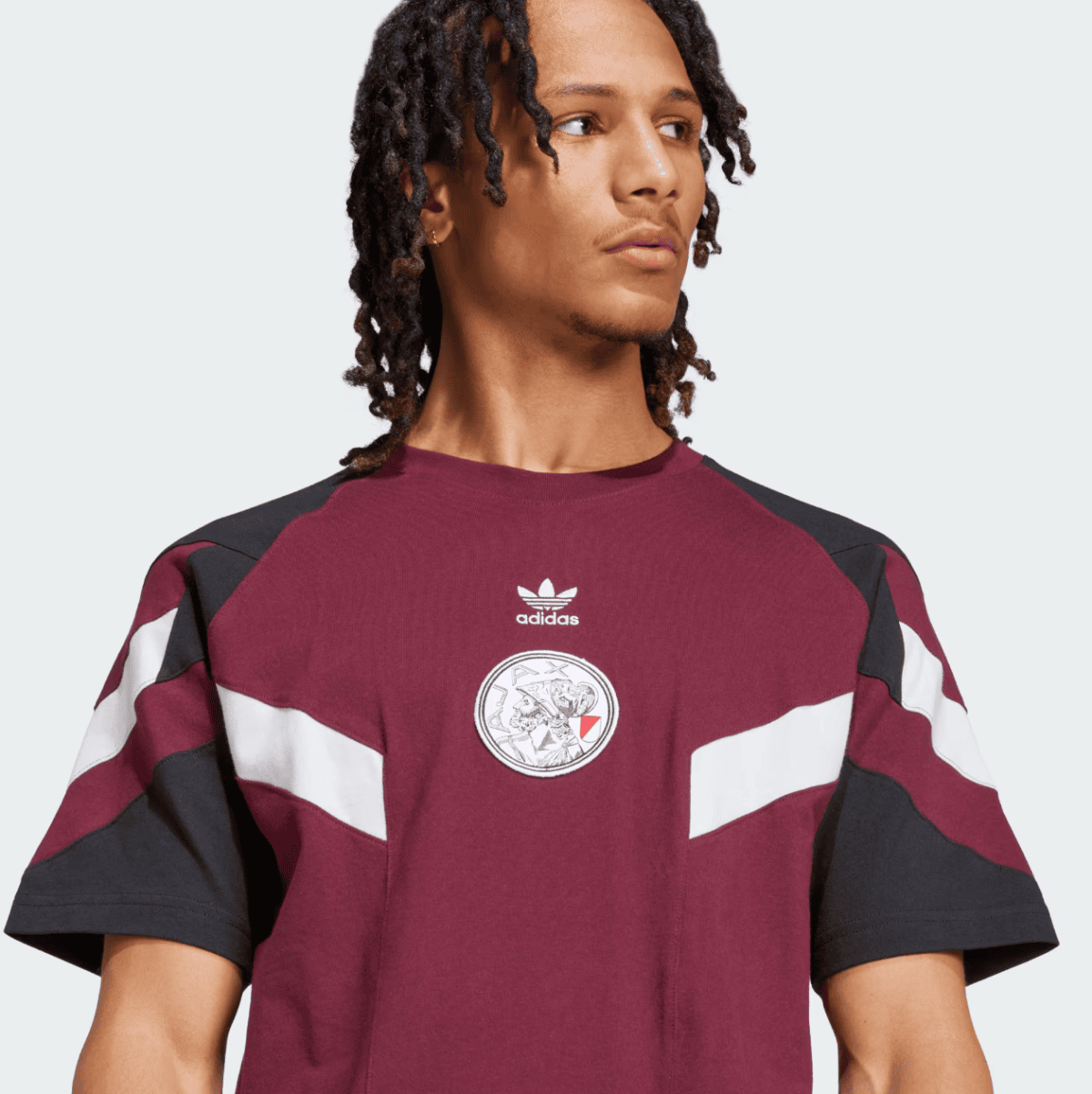Portrait of a man wearing a maroon Adidas t-shirt with black and white color-block sleeves and a small Adidas logo on the chest.