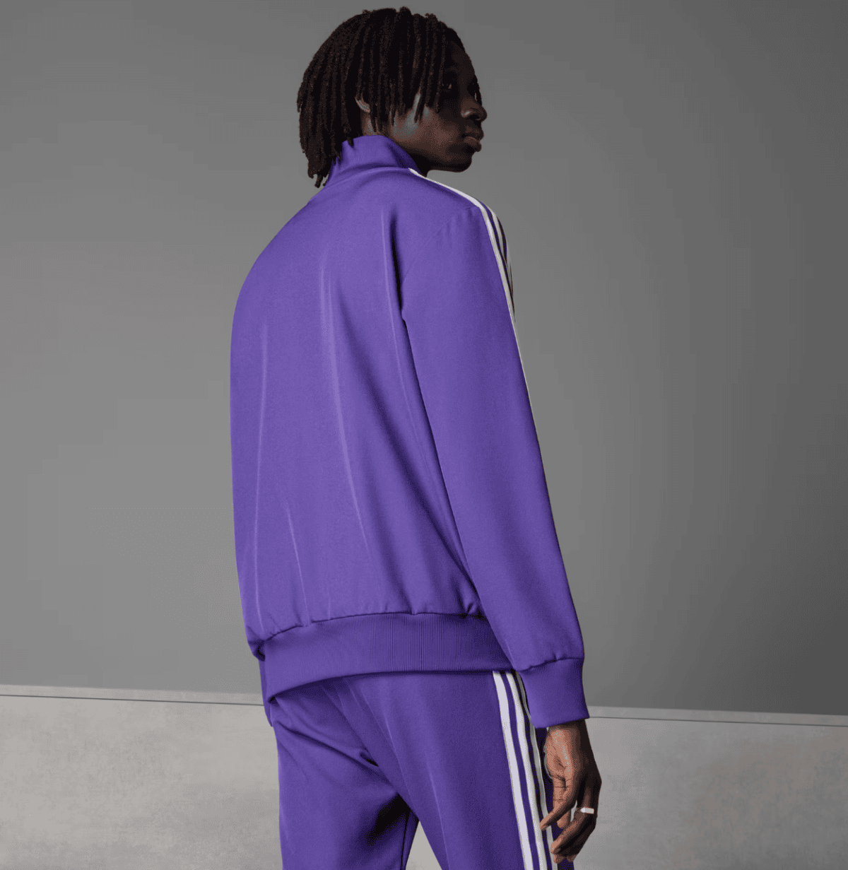 Back view of a person wearing a purple tracksuit with white stripes against a gray backdrop.