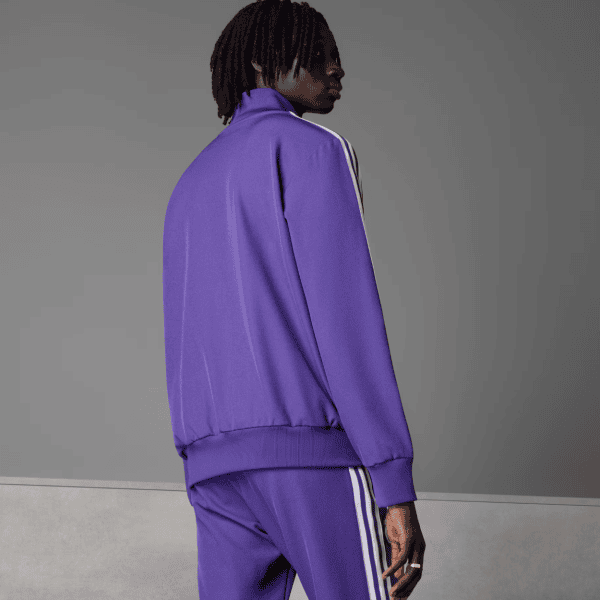 Back view of a person wearing a purple tracksuit with white stripes against a gray backdrop.
