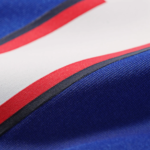 Close-up of blue fabric with a white stripe edged in red and a dark seam between colors.