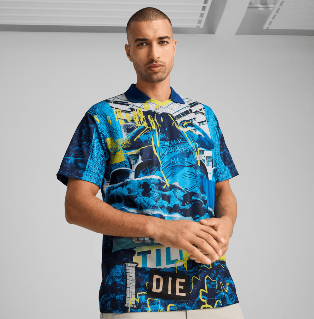 Male model in a vibrant blue and neon yellow graphic shirt with abstract cityscape patterns against a gray studio background.