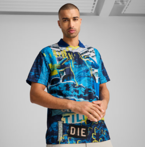 Male model in a vibrant blue and neon yellow graphic shirt with abstract cityscape patterns against a gray studio background.
