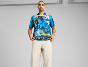 Man standing in a studio wearing a vibrant blue graphic polo shirt and light beige trousers.