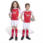 Two smiling children in Arsenal youth soccer kits pose with a ball between them, red jerseys and white shorts.