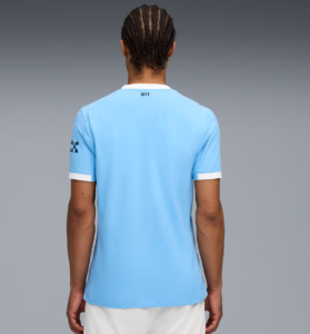 Person with braided hair wearing a light blue soccer jersey, seen from the back with white collar and sleeve cuffs.