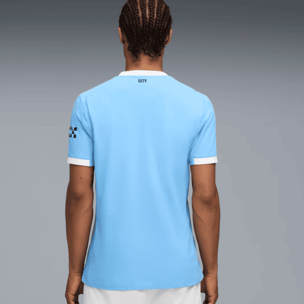 Person with braided hair wearing a light blue soccer jersey, seen from the back with white collar and sleeve cuffs.