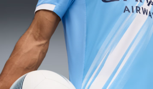 Close-up of a soccer player’s arm in a light blue jersey holding a white soccer ball.