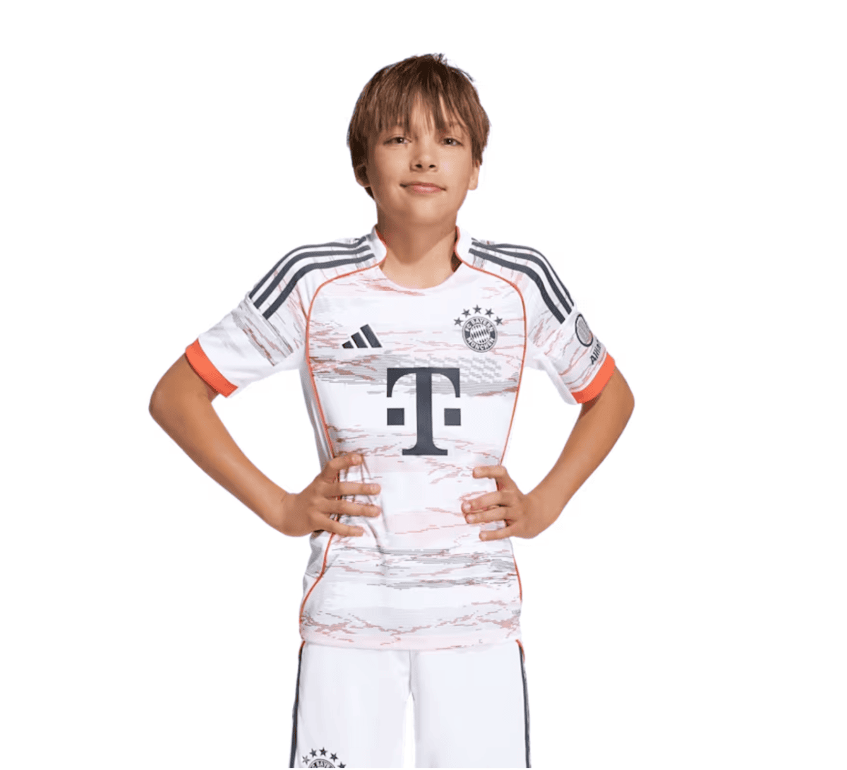 Young boy wearing a white Bayern Munich football jersey with black and orange accents, standing with hands on hips, smiling.