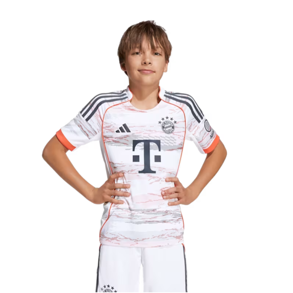 Young boy wearing a white Bayern Munich football jersey with black and orange accents, standing with hands on hips, smiling.