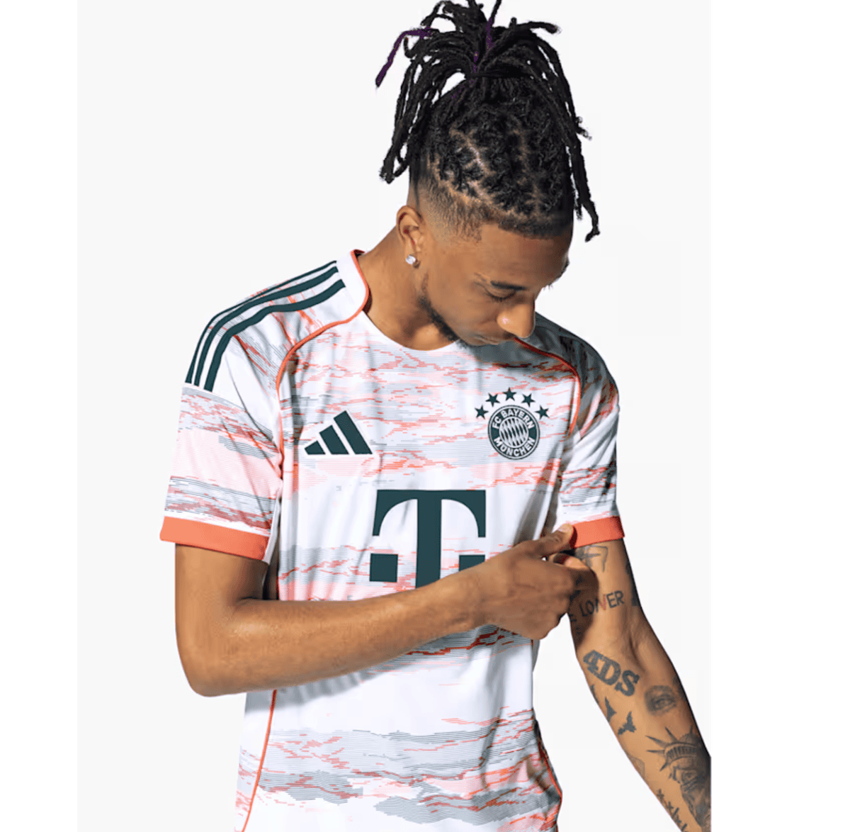 Young man with braided hair wearing a Bayern Munich jersey, looking down at his tattooed forearm.