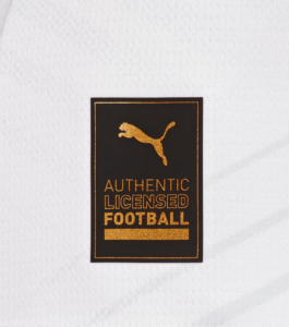 Black rectangular label with a gold Puma logo and the text 'AUTHENTIC LICENSED FOOTBALL' on white fabric.