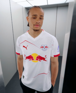 Portrait of a young man in a white RB Leipzig football jersey posing in an elevator or narrow hallway.