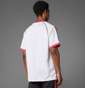Back view of a person wearing a white jersey with red trim on sleeves and collar, standing against a gray background