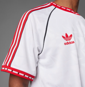 White Adidas sports jersey close-up, featuring red three-stripe detailing along the shoulder and a red Adidas trefoil logo on the back.
