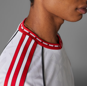 Close-up of a person’s neck and shoulder wearing a white sports jersey with red stripes and a thin gold chain.