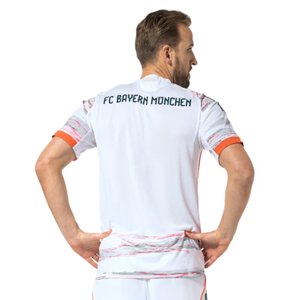 Back view of a man wearing a white FC Bayern Munich football jersey with orange trim on sleeves and hem, hands on hips.