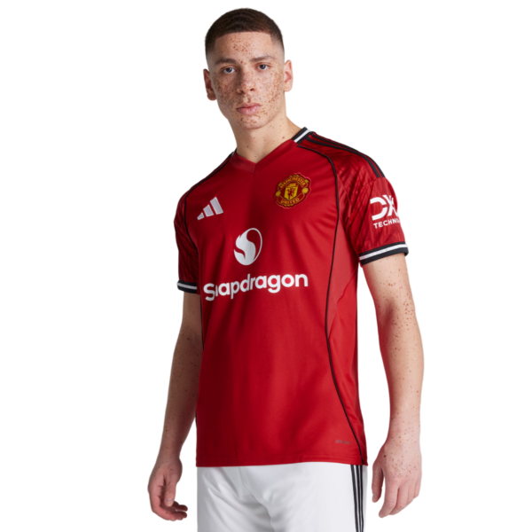 Manchester United red football shirt with Snapdragon sponsor logo on front, badge on chest, black piping, and white shorts against a white background.