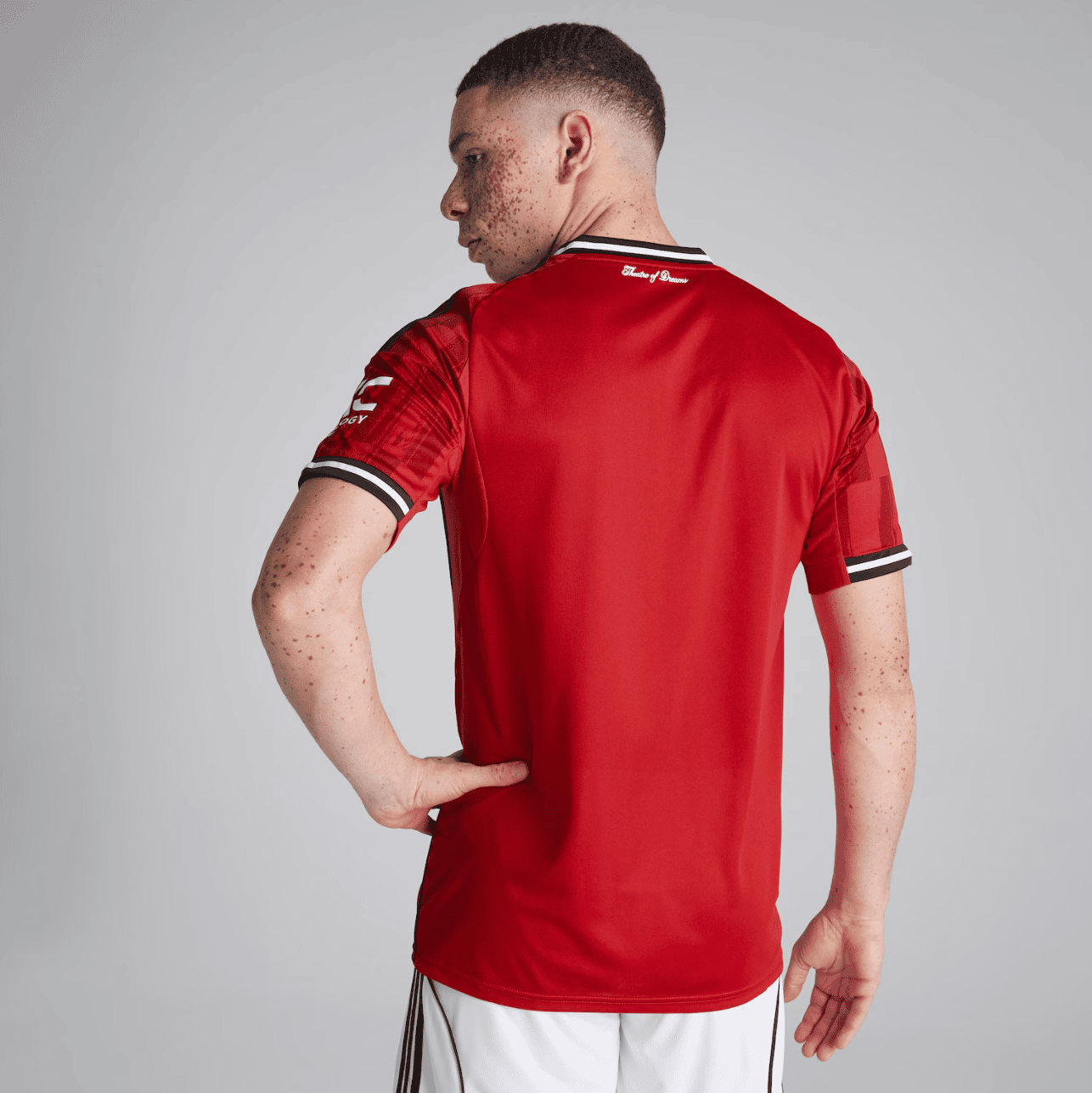Screenshot_2025-06-23_193707 | UAE SPORT STORE Rear view of a man in a red sports jersey with black-and-white trim, standing with one hand on his hip against a grey studio backdrop.