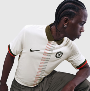 Screenshot_2025-06-23_194633 | UAE SPORT STORE Side profile of a male footballer wearing a Chelsea FC cream jersey with olive collar and red-green sleeve trim, Nike logo visible on chest.