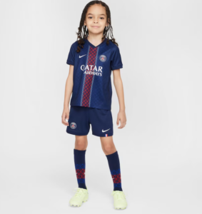 Young girl wearing a Paris Saint-Germain soccer kit in navy, with Qatar Airways sponsor, standing against a light background.