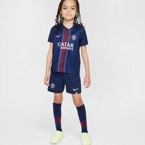 Young girl wearing a Paris Saint-Germain soccer kit in navy, with Qatar Airways sponsor, standing against a light background.