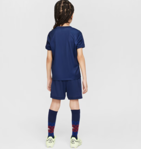 Back view of a child in a navy soccer kit: jersey, shorts, knee-high navy socks with red geometric pattern, and light-green cleats