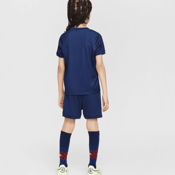 Back view of a child in a navy soccer kit: jersey, shorts, knee-high navy socks with red geometric pattern, and light-green cleats