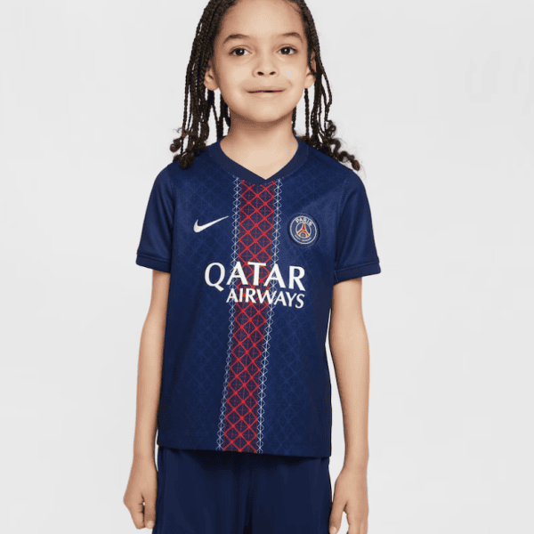 Young girl wearing a navy PSG soccer jersey with a red vertical stripe, sponsor logo, and club crest, standing against a light background.