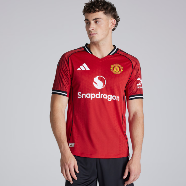 Male model wearing a red Manchester United football jersey with Snapdragon logo and club crest on the chest, facing left.