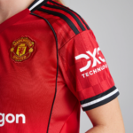 Close-up of a red Manchester United jersey sleeve showing the club crest and DXC Technology logo on the sleeve edge area.