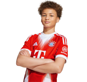 Young boy wearing a red FC Bayern jersey with arms crossed, posing confidently against a white background.